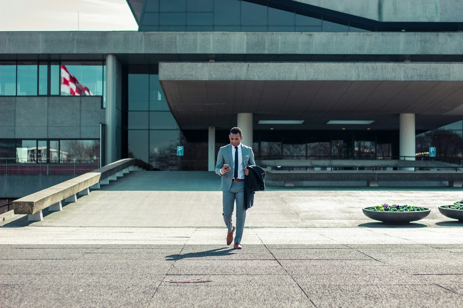 Businessman in a gray suit walking outside a modern building while looking at his phone