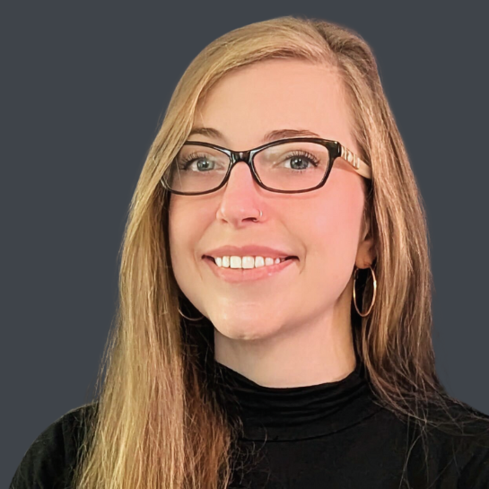 Professional headshot of Maddalena Rae Baker, an immigration paralegal with long blonde hair, glasses, and a warm smile, set against a dark gray background.