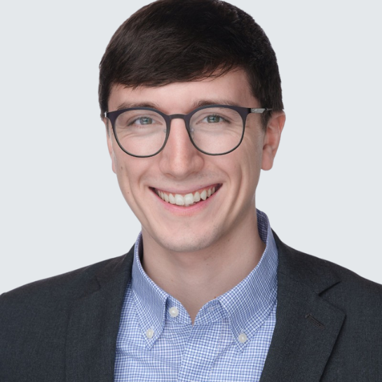Professional headshot of Andrew Wojcik, Legal Operations Analyst at Stelmakh & Associates, wearing glasses, a checkered blue shirt, and a dark blazer, smiling confidently against a light background.