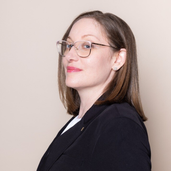Professional headshot of Karen Studeny, Associate Attorney at Stelmakh & Associates, wearing glasses and a black blazer against a neutral beige background.