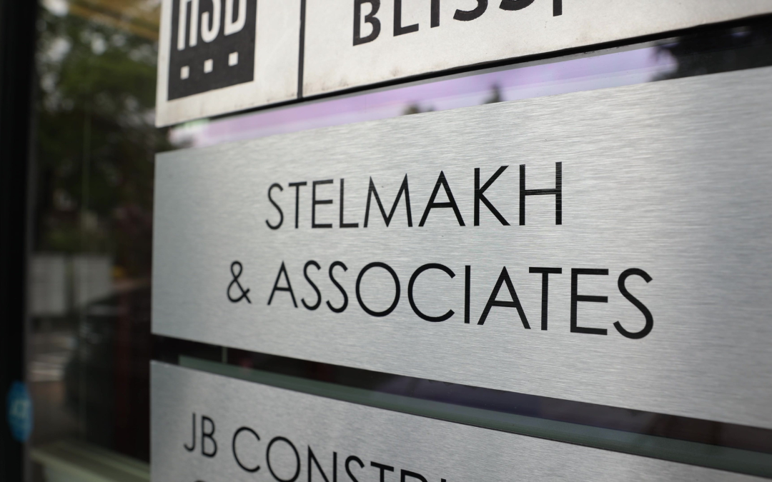 Gros plan de l'enseigne du bureau Stelmakh & Associates sur une plaque en métal brossé à l'extérieur du bâtiment.